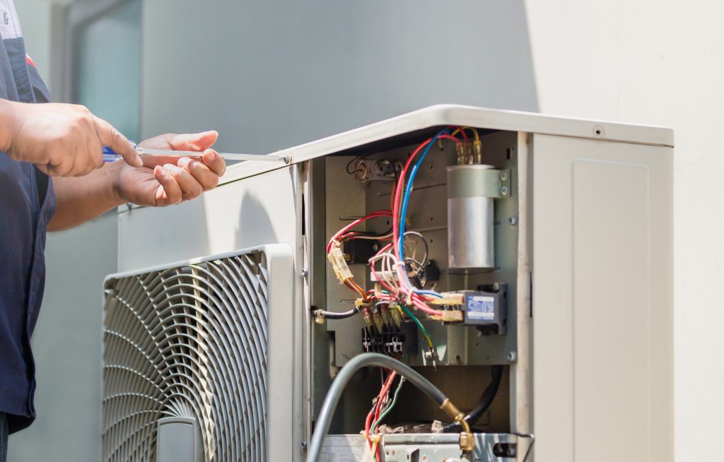 Male technician hands using a screwdriver fixing modern air conditioner, repairing and servicing, Maintenance and repairing concept